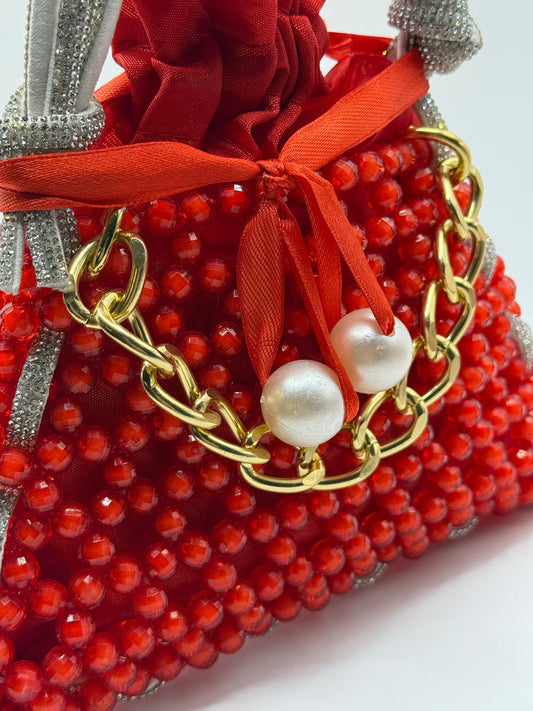 Close-up of Crimson Charm red handbag with textured beads, gold chain, pearl embellishments, and shimmering handles
